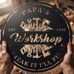 Puede incluir: Un letrero circular de metal negro con texto recortado y siluetas de herramientas. El texto dice "PAPA'S", "EST 1995", "Workshop" y "U BREAK IT I'LL FIX IT". El diseño incluye martillos, llaves inglesas, alicates y taladros dispuestos simétricamente.