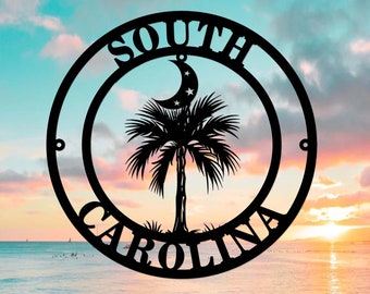 May include: Black metal wall art featuring the South Carolina state symbol. The design includes a crescent moon with stars, a palm tree, and the words "SOUTH CAROLINA" in a circular frame. The art is set against a colorful sunset backdrop.
