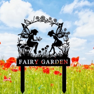 May include: Black metal silhouette of two fairies with wings, sitting in a garden with flowers and the text "FAIRY GARDEN" on a sign.