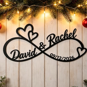 Pode incluir: Uma placa de parede em metal preto com o formato de um símbolo de infinito, apresentando os nomes David e Rachel, um e comercial e a data 09/12/2026. O design inclui dois contornos de coração no topo e um na extremidade direita.