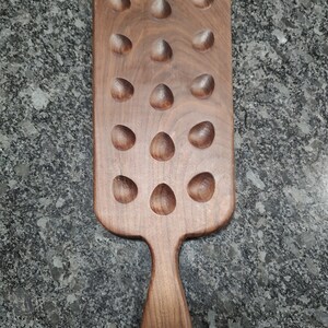 Pode incluir: Uma bandeja de servir de madeira com uma alça e 18 reentrâncias. A bandeja é feita de madeira marrom escura e tem um acabamento natural.