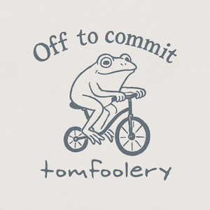 May include: A whimsical illustration features a frog riding a bicycle. The text above reads "Off to commit", and below, "tomfoolery". The design is in a muted blue-gray color, set against a cream background. The frog is smiling.