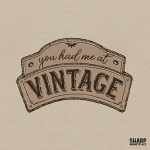 Puede incluir: Una ilustración gráfica de color beige de un letrero con un borde curvo en la parte superior e inferior. El texto dice you had me at en letra cursiva, con la palabra VINTAGE en letras mayúsculas grandes, negritas y de color marrón oscuro. SHARP MARKETPLACE aparece abajo.