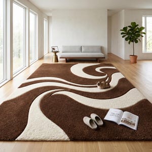 May include: A large, rectangular brown rug with a cream-colored, wavy design. The rug is in a living room setting, with a cat resting on it, along with a pair of slippers and an open book. The room has large windows and a neutral color palette.