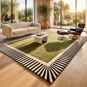 May include: A large rectangular area rug featuring a solid olive green center panel framed by a wide border of alternating black and cream-colored stripes that radiate outward toward the edges of the rug, creating a bold geometric pattern.