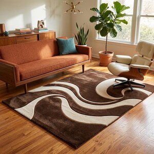 May include: A brown area rug with a cream-colored wave design in a living room setting. The rug is placed on a hardwood floor, with a mid-century modern sofa, chair, and plants in the background. The room is well-lit with natural light.