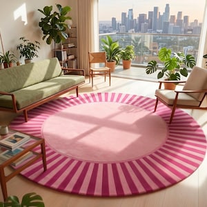 Puede incluir: Una alfombra redonda rosa con un borde a rayas en un sal&oacute;n. La alfombra presenta un centro rosa m&aacute;s claro y un patr&oacute;n de rayas rosa m&aacute;s oscuro alrededor del borde. La habitaci&oacute;n incluye un sof&aacute; verde, sillas y plantas en macetas.