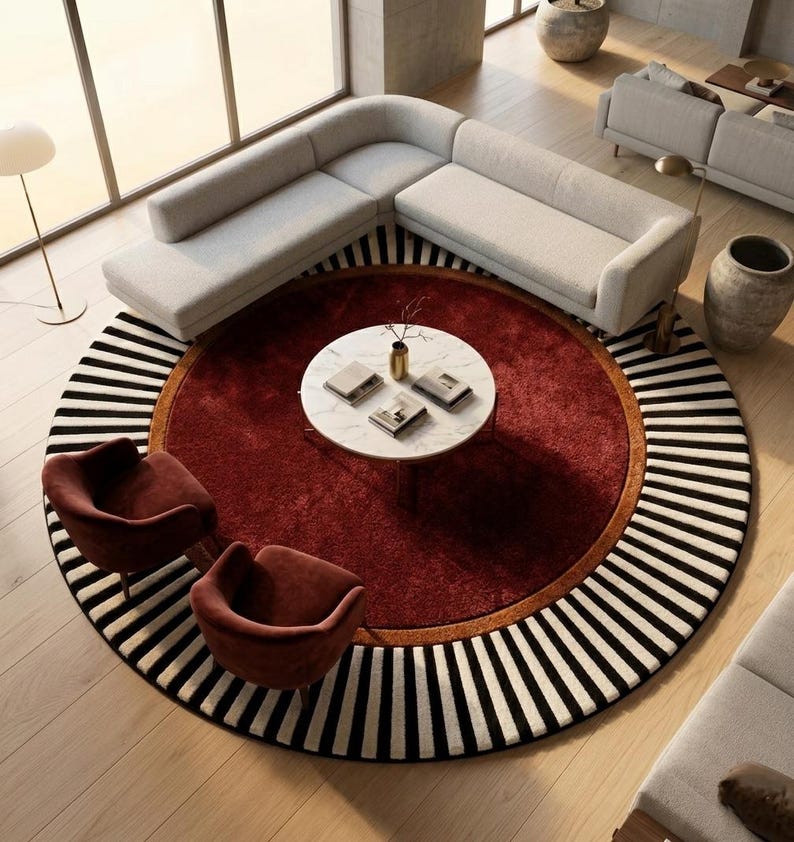 Puede incluir: Vista a&eacute;rea de un sal&oacute;n moderno con una alfombra grande y redonda. La alfombra tiene un centro rojo oscuro, un borde marr&oacute;n y un borde exterior a rayas blancas y negras. Dos sillones burdeos frente a una mesa de centro blanca.