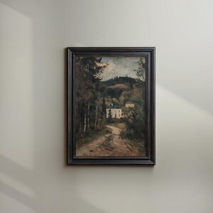 May include: Framed landscape painting depicting a dirt road leading to a white house nestled among trees. The artwork features a dark wooden frame and a muted color palette of greens, browns, and grays, evoking a serene, natural scene.