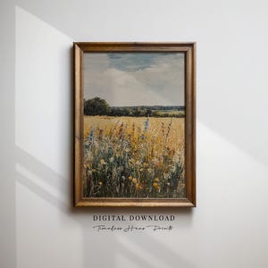Puede incluir: Una pintura de paisaje enmarcada representa un campo de trigo dorado y flores silvestres bajo un cielo nublado. La obra de arte tiene un marco de madera y el texto "DIGITAL DOWNLOAD" y "Timeless Home Prints". La pintura evoca una sensación de tranquilidad.
