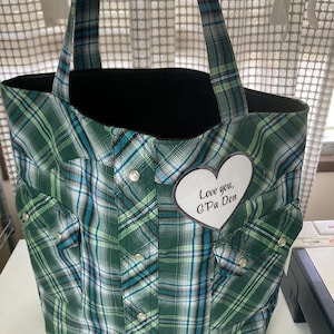May include: A green plaid tote bag with black lining and matching handles. The bag features a repurposed shirt design with pockets and snap closures. A white heart-shaped patch with the text "Love you, G'Pa Don" is sewn on the front.