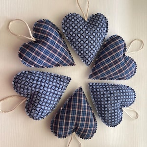May include: Six stuffed fabric hearts arranged in a circle, each featuring a hanging loop. Three hearts have a blue and white geometric pattern, while the other three display a blue, white, and brown plaid design with scalloped edges.
