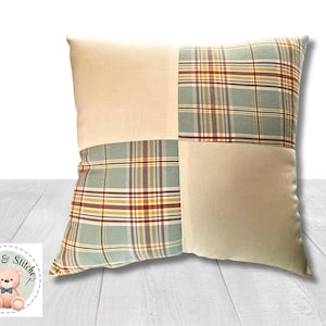 May include: A square throw pillow featuring a patchwork design with alternating panels of solid cream fabric and a plaid pattern in shades of sage green, mustard yellow, and dark red. The pillow has a clean, simple construction.