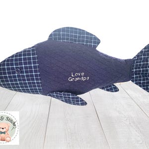 May include: A plush fish toy crafted from navy blue fabric with a quilted texture and a dark blue and white grid pattern on the head, fins, and tail. A small button serves as an eye, and the text Love Grandpa is embroidered in white thread.