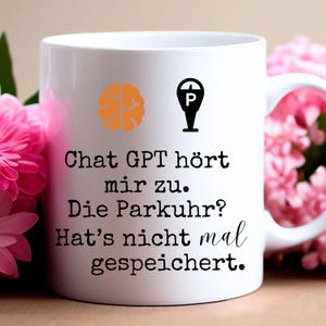 Könnte beinhalten: Weiße Keramiktasse mit einem schwarz-weißen Parkuhr-Symbol und einem Gehirn-Symbol in Orange. Die Tasse hat schwarzen Text, der lautet "Chat GPT hört mir zu. Die Parkuhr? Hat's nicht mal gespeichert."
