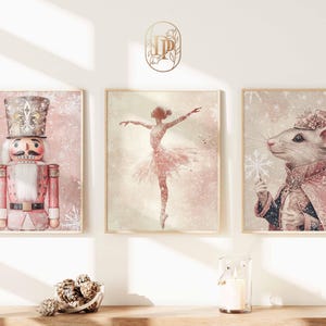 May include: Three framed art prints with a winter theme. The prints feature a nutcracker, a ballerina, and a mouse in a coat, all in a soft pink and white color palette. The art has a vintage, watercolor style.