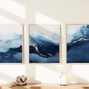 May include: Three abstract paintings in gold frames, each depicting a blue and gold wave with a white background.