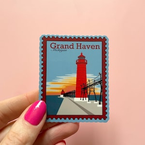 May include: A blue and red sticker with a vintage stamp design featuring a lighthouse and pier with the text "Grand Haven, Michigan".