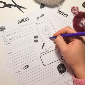 Może przedstawiać: Scena rękodzieła z naszkicowanym kapturem na arkuszu wzoru. Arkusz zawiera szczegóły, takie jak rodzaj przędzy, rozmiar szydełka i miejsce na notatki. Widoczna jest również kulka przędzy, nożyczki i długopis. Rozmiar szydełka to 3,5 mm.