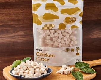 Puede incluir: Una bolsa blanca resellable de golosinas para perros Waita Chicken Cubes. La bolsa está sobre una superficie de madera con un pequeño cuenco de golosinas y hojas verdes.