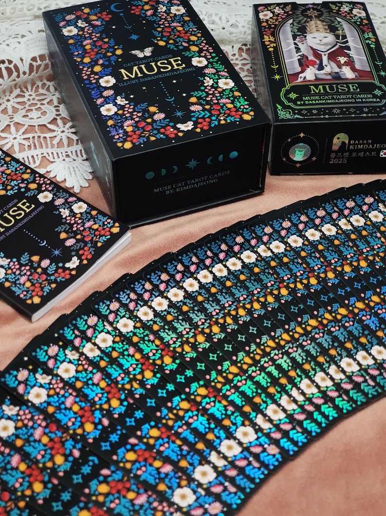 K&ouml;nnte beinhalten: Ein Set "Muse Cat Tarot Cards" mit floralen und himmlischen Designs. Die schwarzen Schachteln und Kartenr&uuml;ckseiten zeigen bunte Blumen und das Wort "MUSE". Die Karten sind aufgef&auml;chert und zeigen komplizierte Muster. Der Text "MUSE CAT TAROT CARDS BY KIMDAJEONG" ist sichtbar.