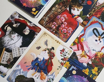 May include: A collection of illustrated tarot cards featuring cats in traditional Asian attire. The cards have vibrant colors, including red, blue, and gold, with floral and geometric patterns. The deck includes a box with a lotus flower design.