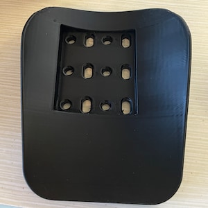 May include: Black plastic mold with a grid of circular holes. The mold is curved and has a smooth surface.