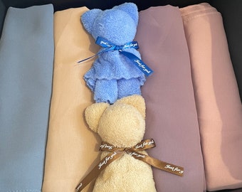 May include: A gift box containing three scarves in shades of blue, beige, and purple. The scarves are arranged in a stack with a blue plush teddy bear on top and a beige plush teddy bear in the middle. The teddy bears have brown ribbons tied around them with the text "Just for you" printed on the ribbons.