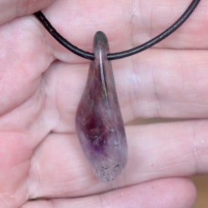 May include: A purple and black amethyst crystal pendant on a black leather cord.