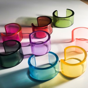 Op de afbeelding: Een set van acht kleurrijke, doorschijnende plastic armbanden. De armbanden zijn allemaal in verschillende kleuren, waaronder groen, roze, paars, blauw en geel.