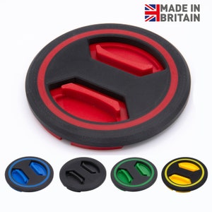 Puede incluir: Un producto circular negro y rojo con un diseño en relieve y un anillo de acento rojo. El producto tiene dos secciones elevadas en el centro. Se muestran variaciones de color adicionales: azul, negro, verde y amarillo.