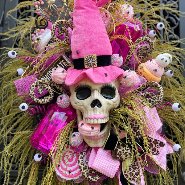 Sweet candy Halloween front door wreath decor with skull witch’s pink hat, macaroons, jewels, lollipop, chocolate bars, spooky cup cakes,