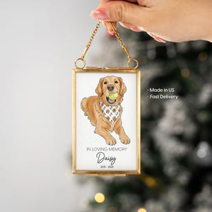 May include: A framed illustration of a Golden Retriever dog holding a tennis ball. The dog is wearing a bandana. The frame is gold-colored and has a chain for hanging. Text on the image reads "In Loving Memory Daisy 2015-2025."