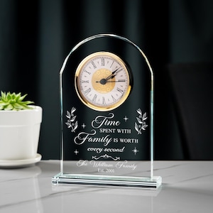 May include: A clear glass clock with a gold-colored clock face and Roman numerals. The clock has the words "Time spent with Family is worth every second" and "The William Family Est. 2001" engraved on it.