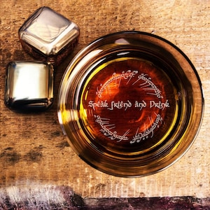 May include: A glass of amber-colored liquid with a circular inscription in Elvish script that reads "Speak Friend and Drink". The glass is on a wooden surface with two silver ice cubes.