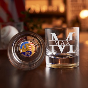 May include: Two clear glass tumblers. One tumbler is upright, displaying the etched name "MAX IVI". The other tumbler is on its side, revealing a commemorative coin with a colorful design featuring the Capitol Building and the Liberty Bell. The coin reads "250th Anniversary".