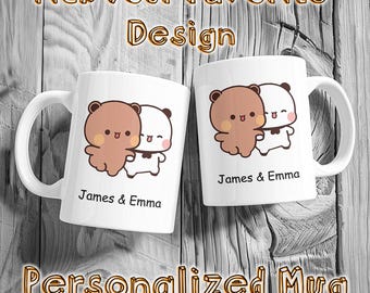 May include: Two white ceramic mugs with brown handles. Each mug features a cartoon illustration of a brown bear and a white panda hugging. The text "James & Emma" is printed on each mug.