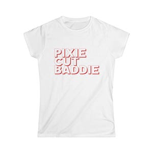 May include: A white short-sleeved t-shirt featuring the text PIXIE CUT BADDIE printed in bold red capital letters with a subtle drop shadow effect centered on the chest area of the garment.