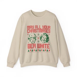 May include: A cream-colored sweatshirt with a festive design. The text reads "MAY ALL YOUR CHRISTMASES + BEA WHITE" in red, with images of two women's faces. Green Christmas trees are at the bottom.