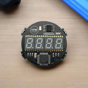 May include: A black electronic circuit board with the text "TPW the printable watch" and "DIGIduino". The board features four digital number displays showing "8.8.8.8".