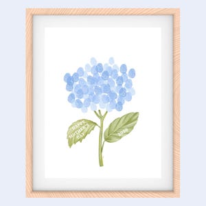 Pode incluir: Impressão emoldurada com uma flor de hortênsia azul feita de impressões digitais. O caule e as folhas são verdes, com o texto "HAPPY MOTHER'S DAY" e o ano "2026" nas folhas. A moldura é castanho-claro.