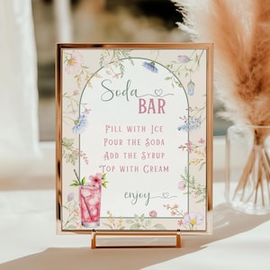 May include: A framed sign with a gold border, featuring the words "Soda Bar" and instructions for making a soda. The sign is decorated with floral illustrations in pink, blue, and green. A glass of soda is pictured.