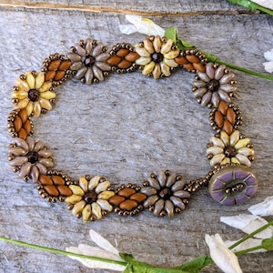 May include: A beaded bracelet with a floral design in shades of brown, beige, and cream. The bracelet features a purple button closure.