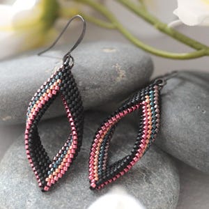 May include: A pair of dangle earrings featuring a marquise-shaped frame constructed from small, woven beads. The beads are arranged in a gradient pattern of matte black, metallic pink, and iridescent blue, suspended from dark metal ear wires.
