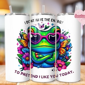 May include: White tumbler with a green frog wearing sunglasses and surrounded by flowers. The text on the tumbler reads "I don't have the energy to pretend I like you today."