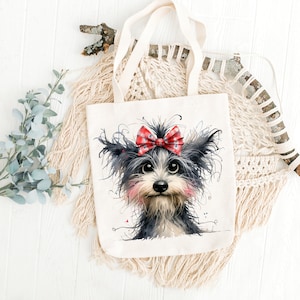 May include: A white tote bag with a black and white illustration of a dog wearing a red and white bow. The dog has a pink nose and black eyes.