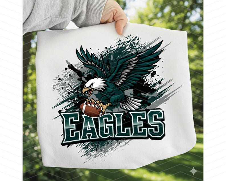 May include: White fabric featuring a detailed graphic of a soaring eagle clutching a football. The eagle is rendered in shades of green, black, and white, set against a backdrop of gray paint splatters. The word "EAGLES" is displayed in bold, green and white lettering.