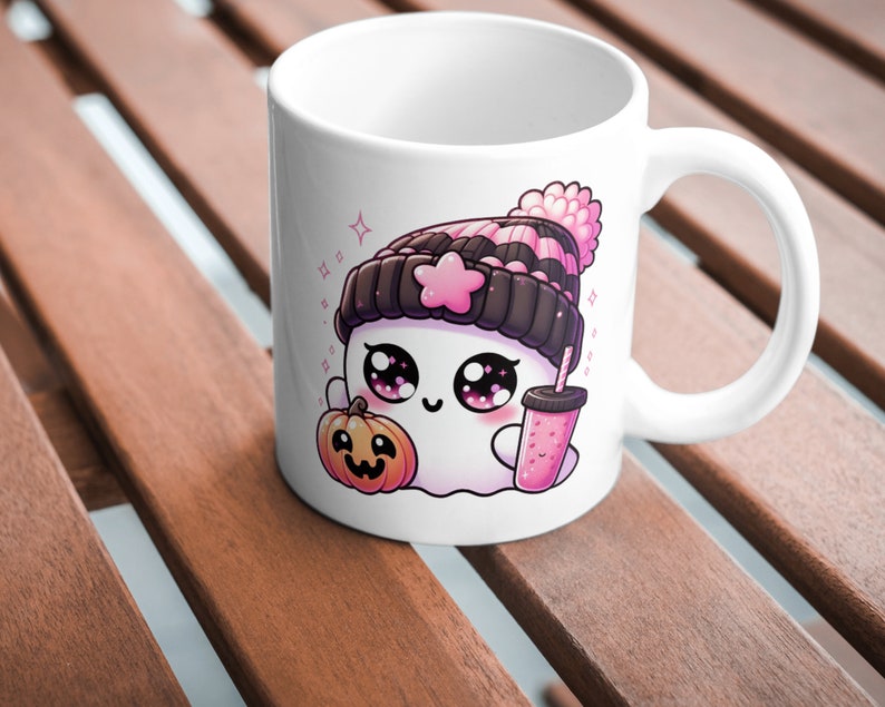 Peut inclure: Mug en c&eacute;ramique blanche avec un fant&ocirc;me de dessin anim&eacute; portant un chapeau ray&eacute; rose et noir, tenant une boisson rose et une petite citrouille orange. Le fant&ocirc;me a de grands yeux et un rougeur rose.