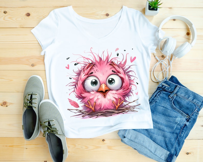 Puede incluir: Camiseta blanca con un p&aacute;jaro rosa de dibujos animados con plumas desordenadas y ojos grandes. El p&aacute;jaro est&aacute; sentado en un nido con algunos corazones rosas en el fondo.