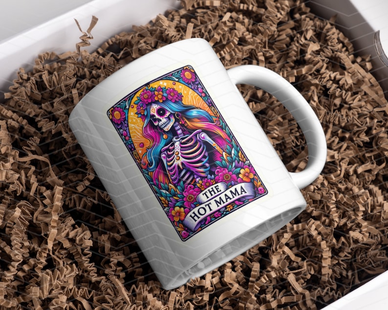 May include: White ceramic mug featuring a colourful illustration of a skeleton with flowers and the text "The Hot Mama".